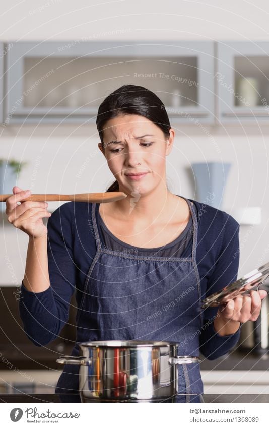 Young cook tasting her food with a grimace Dinner Pot Spoon Face Kitchen Cook Woman Adults 1 Human being 30 - 45 years Hot Anger Food attractive Cooking dislike