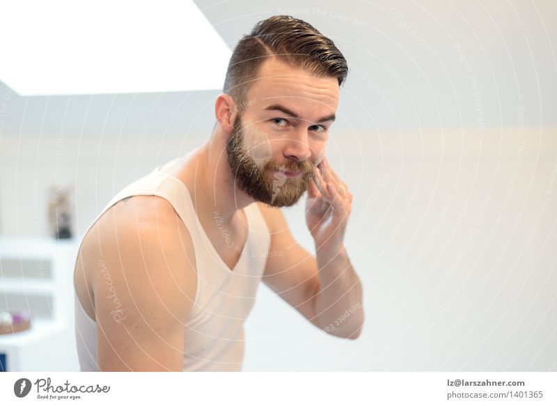 Young man applying shaving cream Face Cream Mirror Bathroom Man Adults Hand Beard Smiling Friendliness Clean Precision appearance care Caucasian Cheek