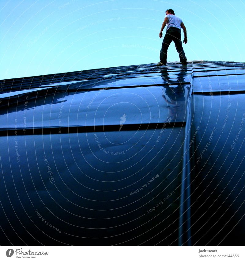 Man balances standing on a slope covered with metal Climbing Monument Tall Above Reflection Worm's-eye view Full-length Rear view height Test of courage Balance