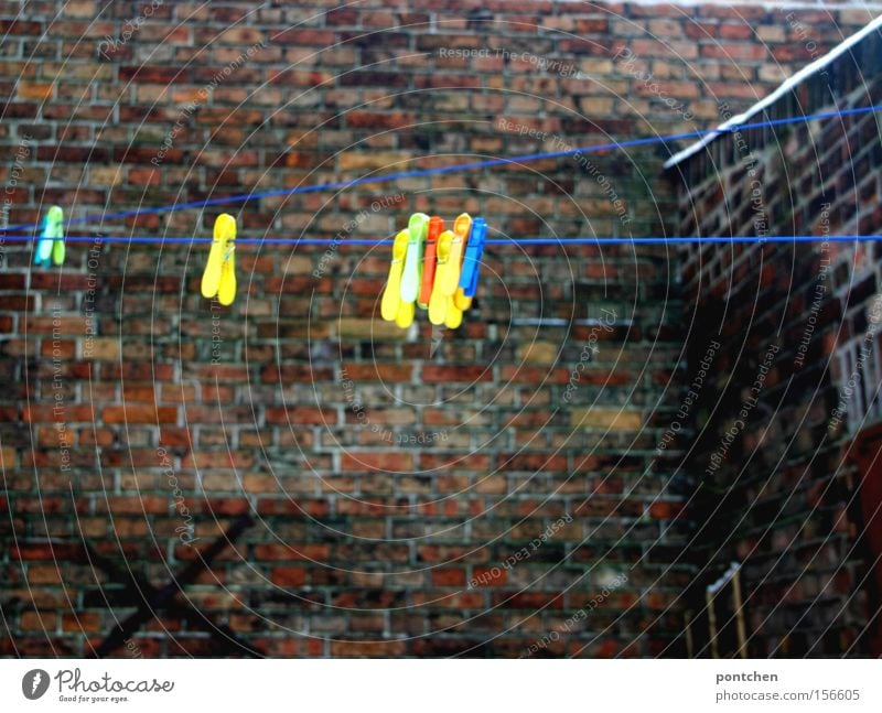 Colorful clothes pegs are hanging from a clothesline in a backyard. Budget Courtyard House (Residential Structure) Brick Wall (barrier) Clothes peg Household