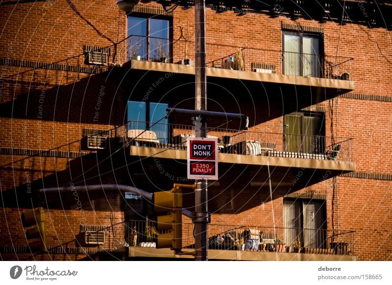 "Don't honk" penalty sign on a lamp post outside a New York red brick apartment building with balconies. Flat (apartment) House (Residential Structure) Window