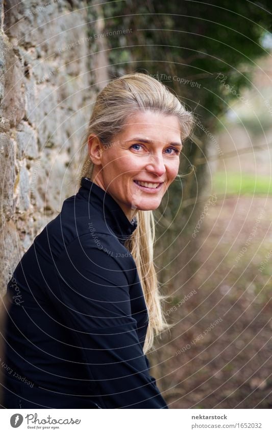 Portrait of female jogger sitting near wall Lifestyle Happy Contentment Calm Human being Woman Adults Blonde Stone Smiling Friendliness Natural Self-confident