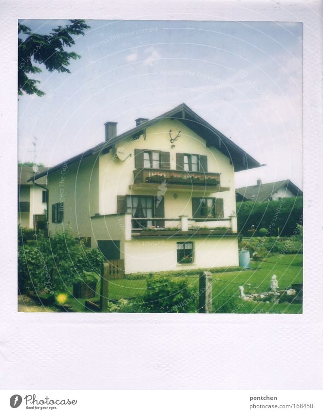 A typical Bavarian detached house with balconies and deer antlers. Houses in the background and garden in the foreground. Settlement in a rural area. Neighbourhood