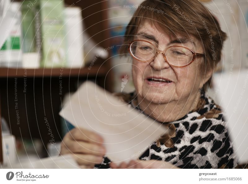 Elderly woman wearing glasses sitting in her living room reading a letter, closeup portrait Lifestyle Face Reading Teacher Retirement Human being Woman Adults