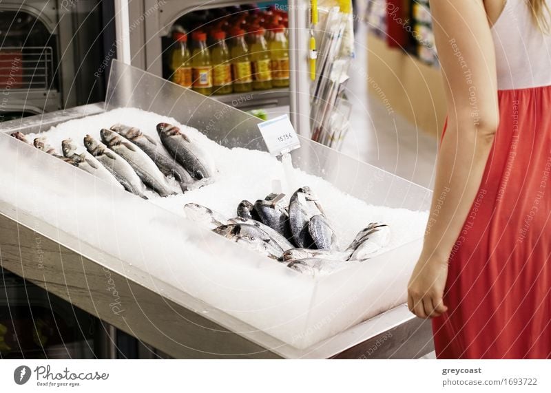 Woman shopping for fish in a supermarket standing looking at a display of fresh whole fish on ice Fish Lifestyle Shopping Happy Human being Young woman