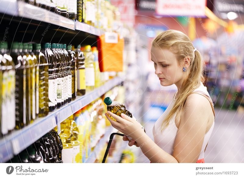 Young blond woman picking an olive oil bottle from the shelves of a supermarket and reading the label Bottle Shopping Young woman Youth (Young adults) Woman