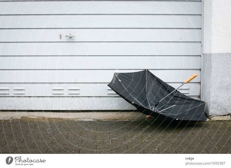 black eyes | German summer Weather Bad weather Wind Gale Rain Deserted Wall (barrier) Wall (building) Facade Garage door Umbrella Gloomy Gray Broken Flying