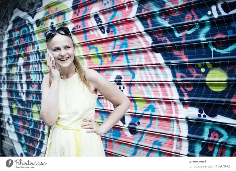 Smiling woman in yellow dress standing and chatting on her smart phone in front of graffiti painted on corrugated iron Lifestyle Style Happy Beautiful Summer