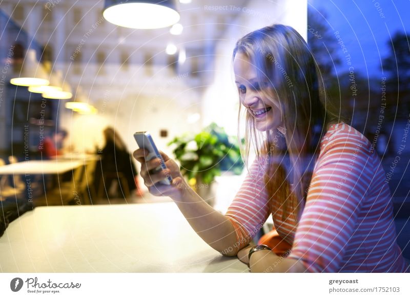 View through the plate glass window with reflections of a young woman sitting in a restaurant using a mobile reading a text message with a smile Happy