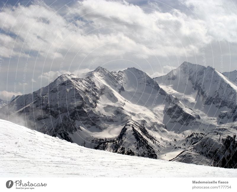 Ski slope and snowy mountain peaks Winter Snow Mountain Winter sports Clouds Alps Snowcapped peak Tall Above Blue Gray Black White Happy Idyll Subdued colour