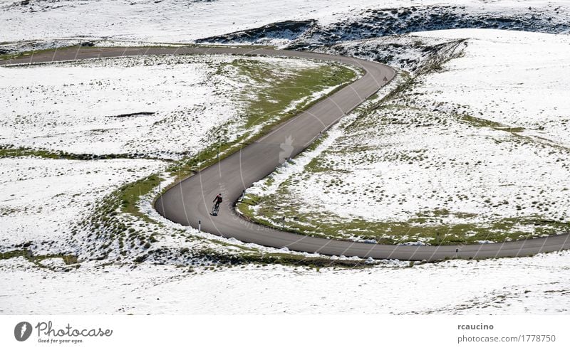 Cyclist goes downhill along a mountain road in a snowy landscape Beautiful Relaxation Vacation & Travel Tourism Trip Summer Winter Snow Mountain Sports Cycling