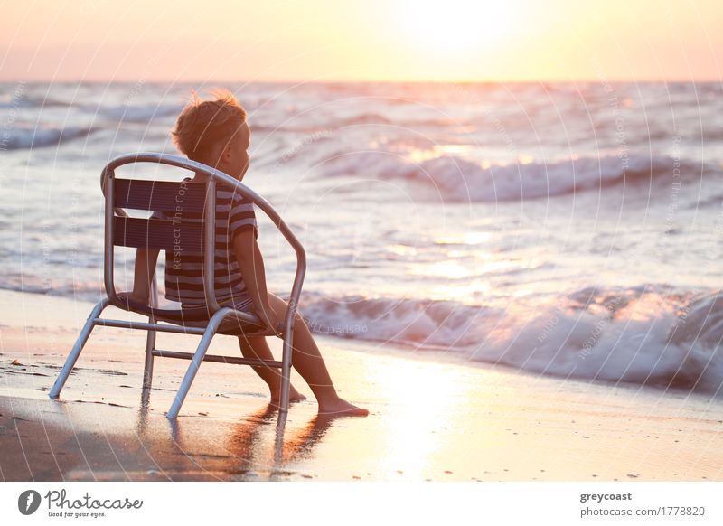 Little boy sitting alone on the chair on the beach and looking at sea waves. Evening sun overshining water Relaxation Vacation & Travel Summer Beach Ocean Chair