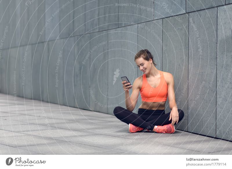 Sporty young woman sitting on forecourt with her mobile Happy Reading PDA Feminine Woman Adults 1 Human being 18 - 30 years Youth (Young adults) Tights Smiling