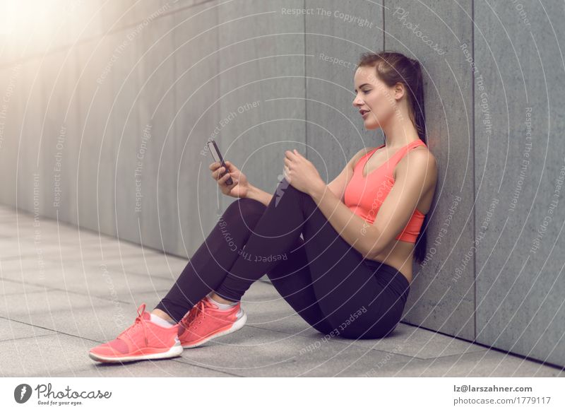 Sporty young woman sitting on forecourt with her mobile Happy Reading PDA Feminine Woman Adults 1 Human being 18 - 30 years Youth (Young adults) Tights Smiling