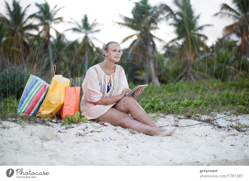 Young smiling woman using tablet computer sitting on the beach after good shopping. Leisure during summer vacation Shopping Exotic Happy Leisure and hobbies