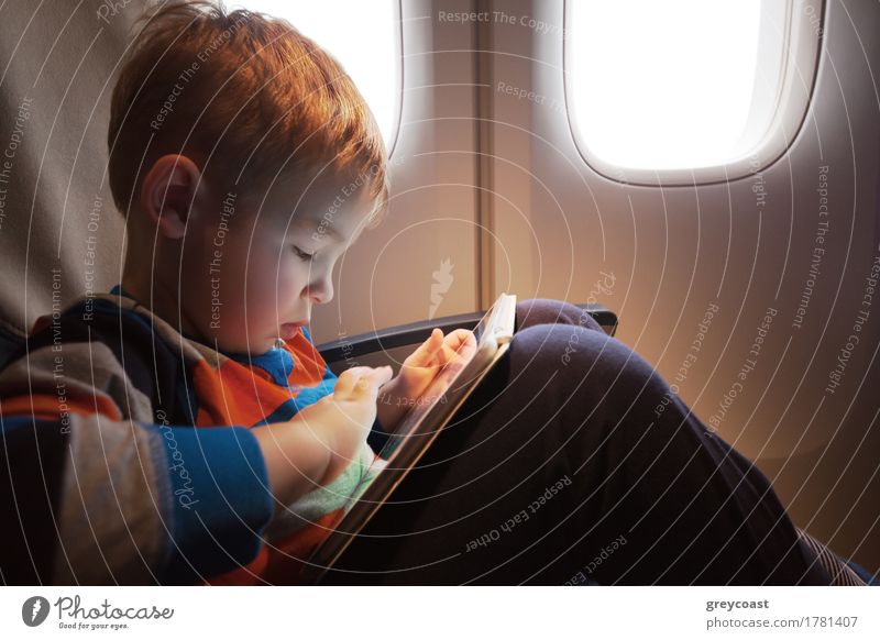 Little child with tablet computer on the lap sitting by the illuminator in the plane Joy Leisure and hobbies Playing Vacation & Travel Trip Entertainment Child