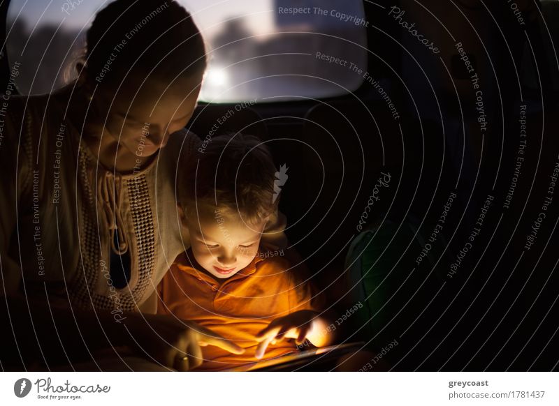 Mother and little son traveling by car at night. They using tablet computer to entertain themselves during trip. Pad screen shining brightly in dark car Playing