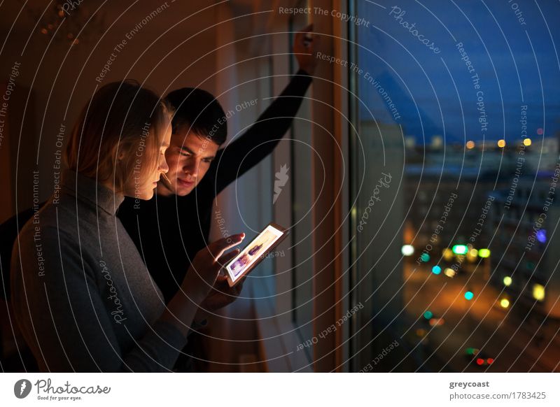 Young people using tablet computer at home. They looking at pictures standing by the window in the evening. City lights outdoor Leisure and hobbies Computer