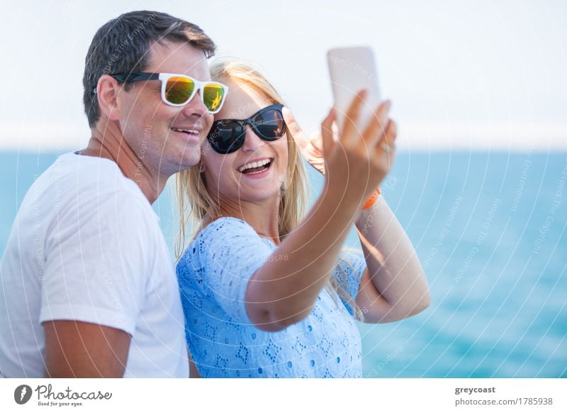 Happy young man and woman in fashionable sunglasses taking cellphone selfie on background of defocused blue sea. Vacation photos Style Vacation & Travel Summer