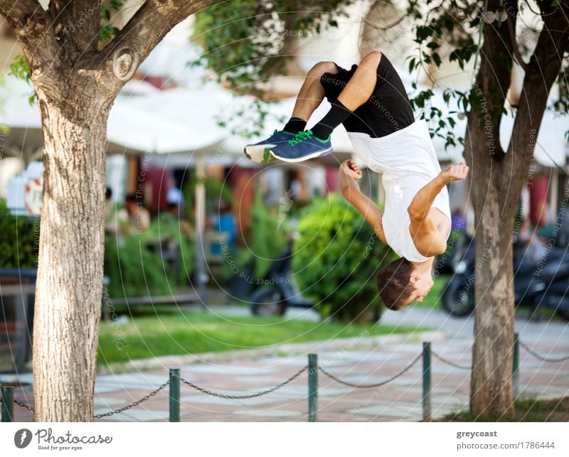 Young extreme athlete doing front flip between the trees. City street with outdoor cafe in background Lifestyle Freedom Summer Sports Human being Man Adults