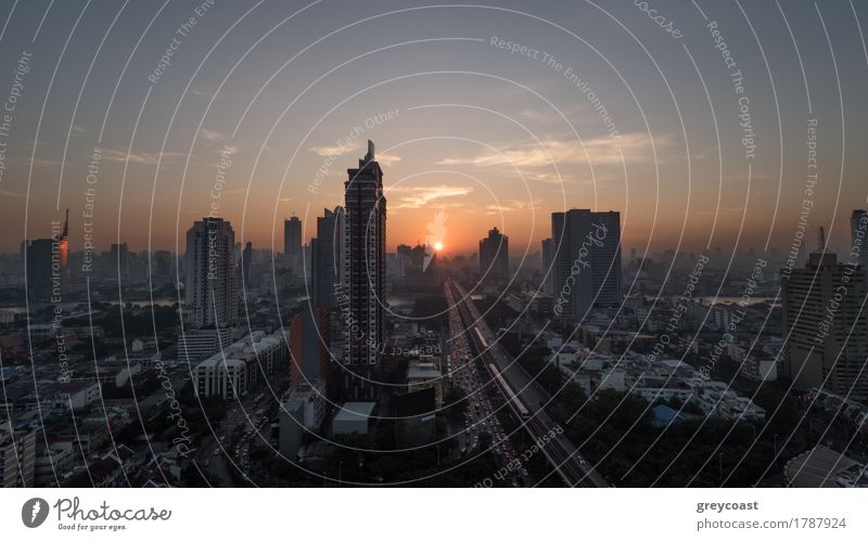 Sunset time in Bangkok, Thailand. City panorama with highrise urban architecture and traffic on highway. Sky in warm colors and sun going down Town High-rise