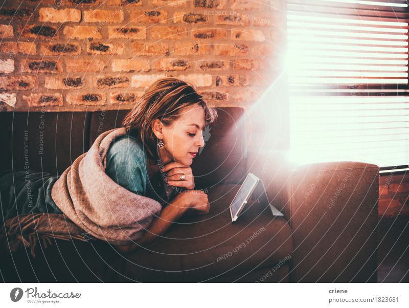 Mature caucasian woman reading newspaper on her digital tablet Lifestyle Relaxation Leisure and hobbies Reading Sofa Living room Work and employment Business