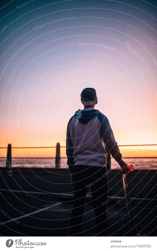 Hipster guy standing on road with longboard watching Sunset Lifestyle Style Joy Leisure and hobbies Freedom Ocean Sports Masculine Young man