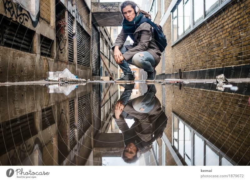 Woman with headphones in side alley in front of puddle in squat Lifestyle Well-being Calm Leisure and hobbies Vacation & Travel Trip Adventure Freedom City trip