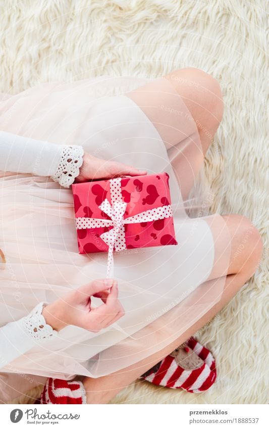 Girl holding Christmas gift on legs and sitting on a carpet Lifestyle Feasts & Celebrations Christmas & Advent Child Human being Hand Legs 1 8 - 13 years