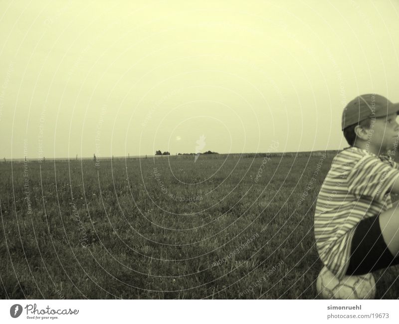 the waiting Boredom Panorama (View) Man Wait Ball Moon Evening Boy (child) Large Foot ball Striped Profile Baseball cap Meadow Pasture Nature Meditative