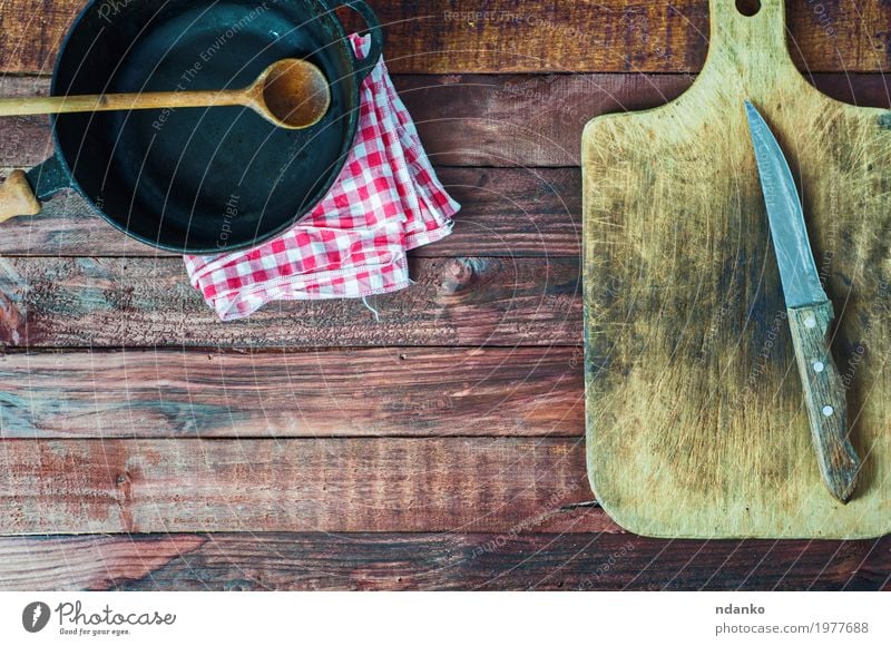 black cast iron pan and cutting board on brown wooden surface Crockery Pan Knives Spoon Table Kitchen Restaurant Tool Cloth Wood Metal Steel Old Above Clean