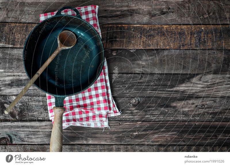 Black frying pan with a spoon on a brown wooden surface Crockery Pan Spoon Table Kitchen Restaurant Tool Cloth Wood Metal Old Above Clean Brown tableware