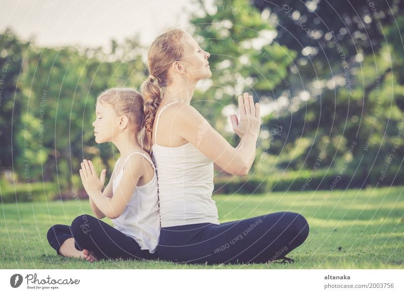 Mother and daughter doing yoga exercises on grass in the park at the day time Lifestyle Joy Happy Beautiful Body Wellness Harmonious Relaxation Meditation