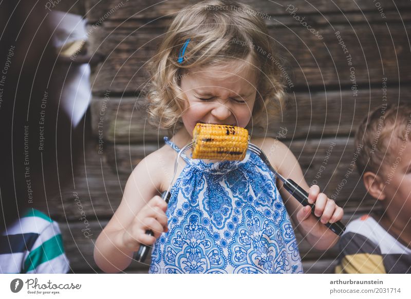 Girl in dress bites into grilled corn in front of a cabin in nature Food Vegetable Maize Corn cob Nutrition Eating Cutlery Fork Healthy Eating