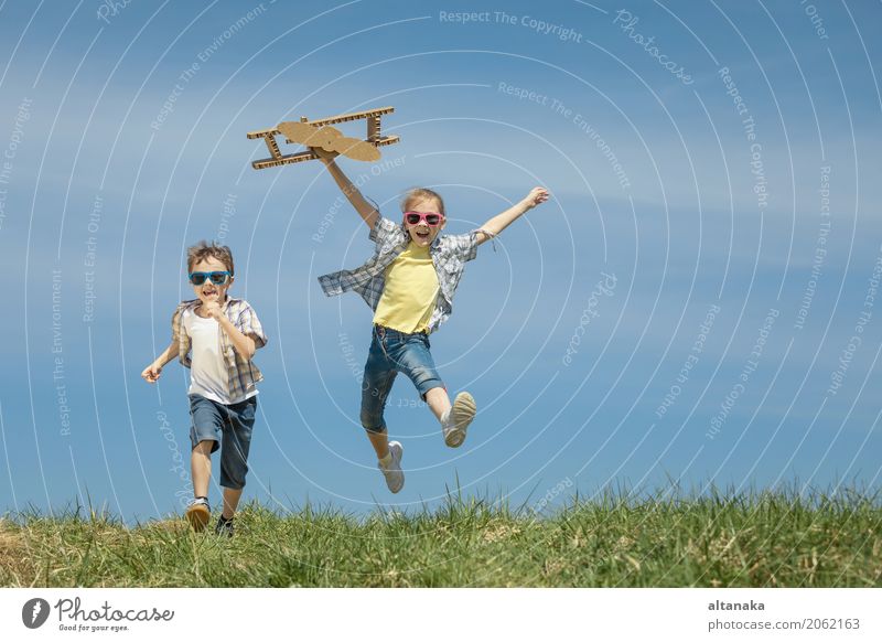 Two little kids playing with cardboard toy airplane in the park at the day time. Concept of happy game. Child having fun outdoors. Picture made on the background of blue sky.