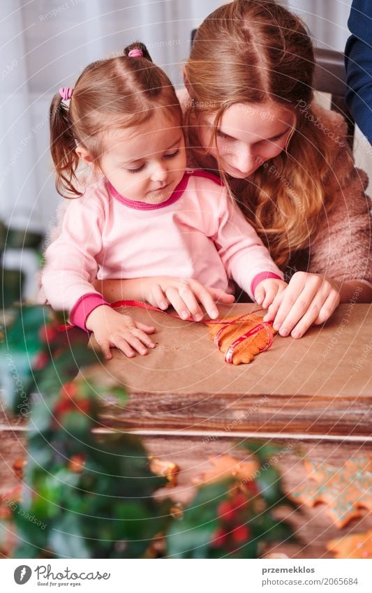 Girls tying baked Christmas gingerbread cookies with ribbon Lifestyle Decoration Table Feasts & Celebrations Christmas & Advent Child Human being Woman Adults