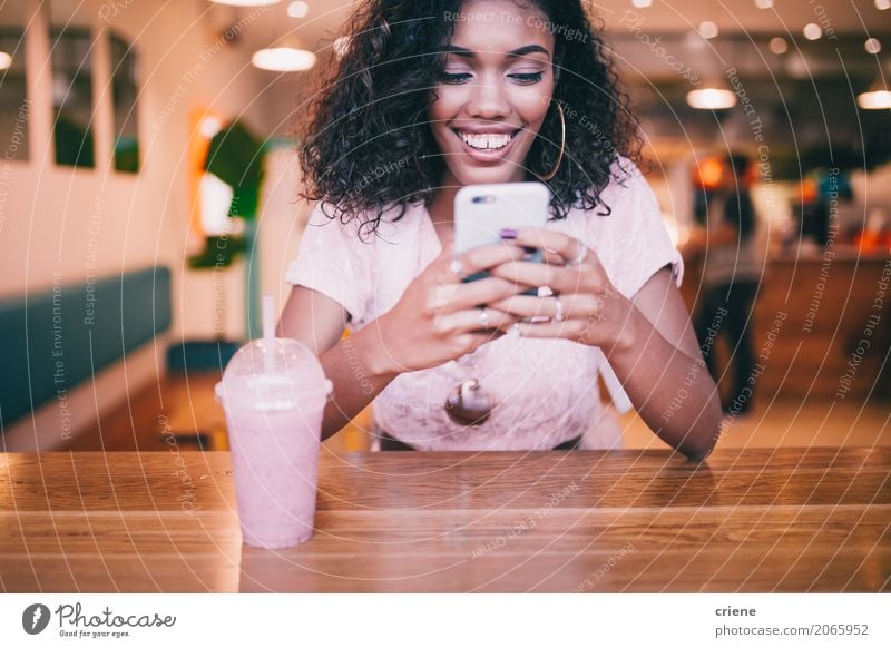 Smiling woman typing message on smartphone in Bar Beverage Drinking Lifestyle Joy Restaurant PDA Technology Internet Youth (Young adults) Email Afro Communicate