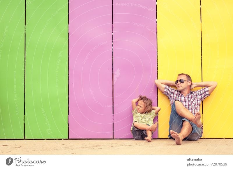 Father and son relaxing near the house at the day time. They sitting near are the colorful wall. Concept of friendly family. Lifestyle Joy Happy Relaxation