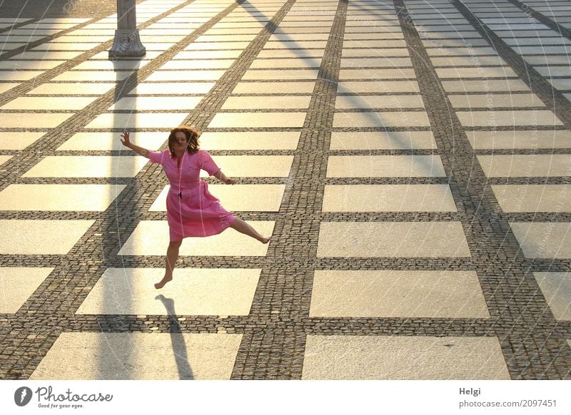 Woman with long brunette hair and pink dress jumping barefoot on a large paved square against the light Human being Feminine Adults 1 45 - 60 years Chemnitz