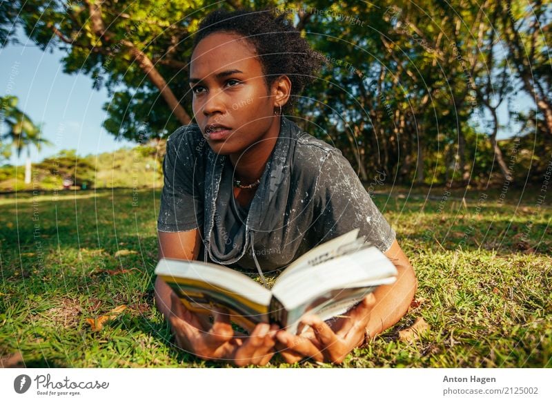 Young afro american woman reading book lying on the green lawn Lifestyle Feminine Young woman Youth (Young adults) 1 Human being 18 - 30 years Adults