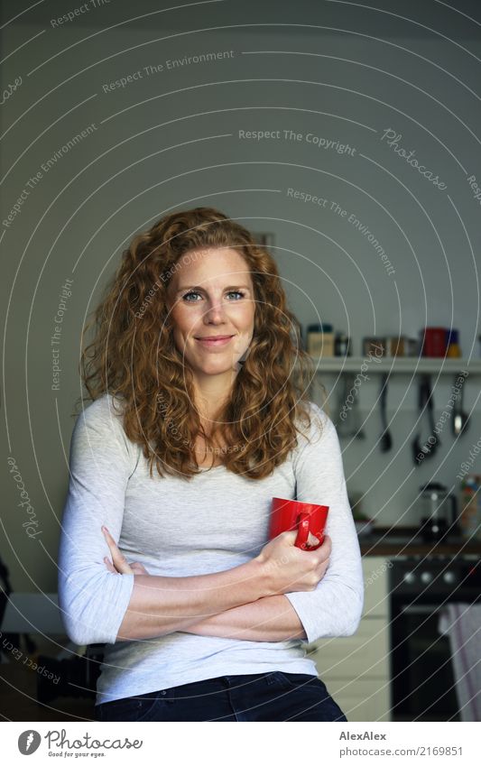 young slim red haired woman with dimples and freckles sits in the kitchen holding a red cup in her hand Hot drink Kitchen Cup Manual cooking appliances Style