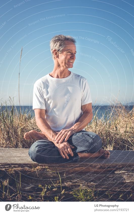 Man sitting in a relaxed yoga pose at the beach. Relaxation Meditation Sun Yoga Adults Old Sit Natural Power Serene 50-60 years Action color image