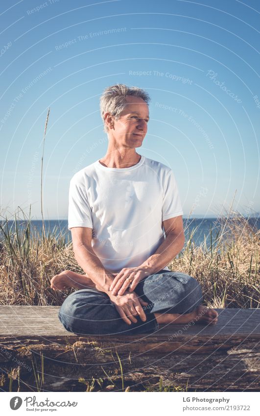 Man sitting in a relaxed yoga pose at the beach. Relaxation Meditation Sun Yoga Adults Old Sit Natural Power Serene 50-60 years Action color image