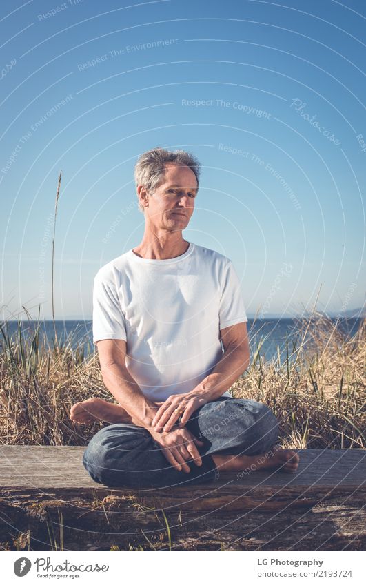 Man sitting in a relaxed yoga pose at the beach. Relaxation Meditation Sun Yoga Adults Old Sit Natural Power Serene 50-60 years Action color image