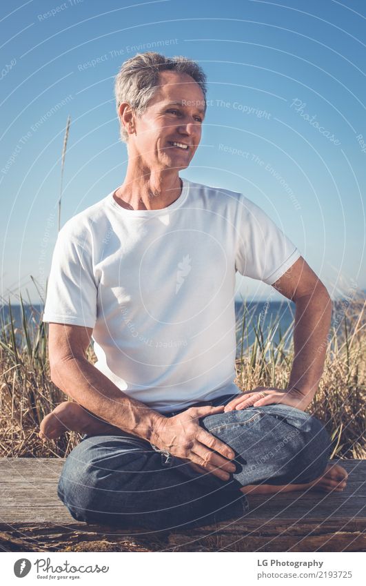 Man sitting in a relaxed yoga pose at the beach. Relaxation Meditation Sun Yoga Adults Old Sit Natural Power Serene 50-60 years Action color image