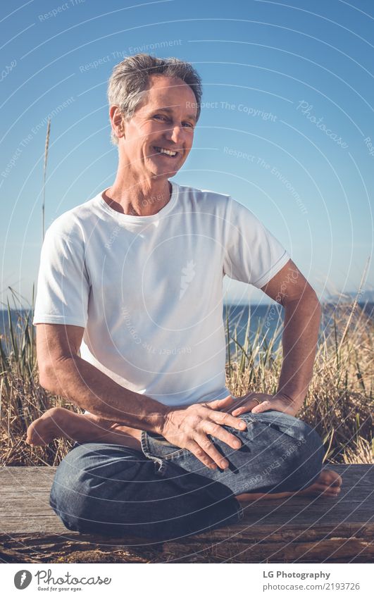 Man sitting in a relaxed yoga pose at the beach. Relaxation Meditation Sun Yoga Adults Old Sit Natural Power Serene 50-60 years Action color image