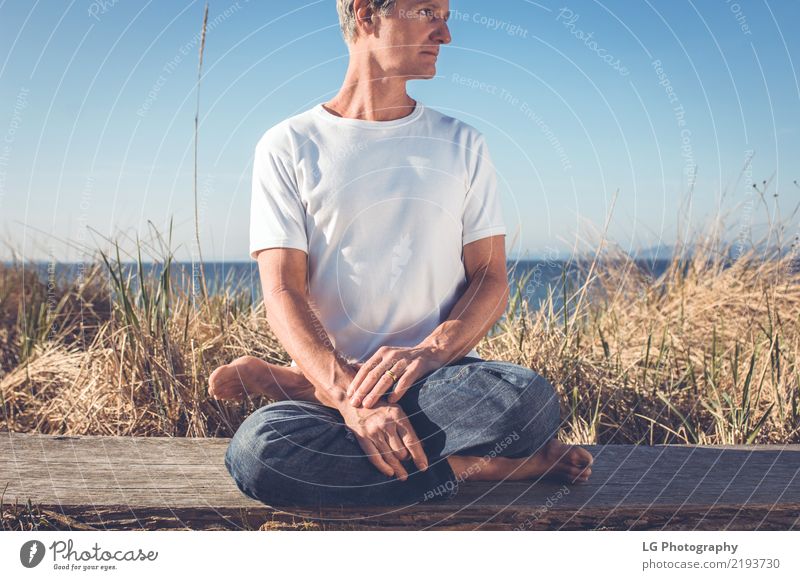 Man sitting in a relaxed yoga pose at the beach. Relaxation Meditation Sun Yoga Adults Old Sit Natural Power Serene 50-60 years Action color image