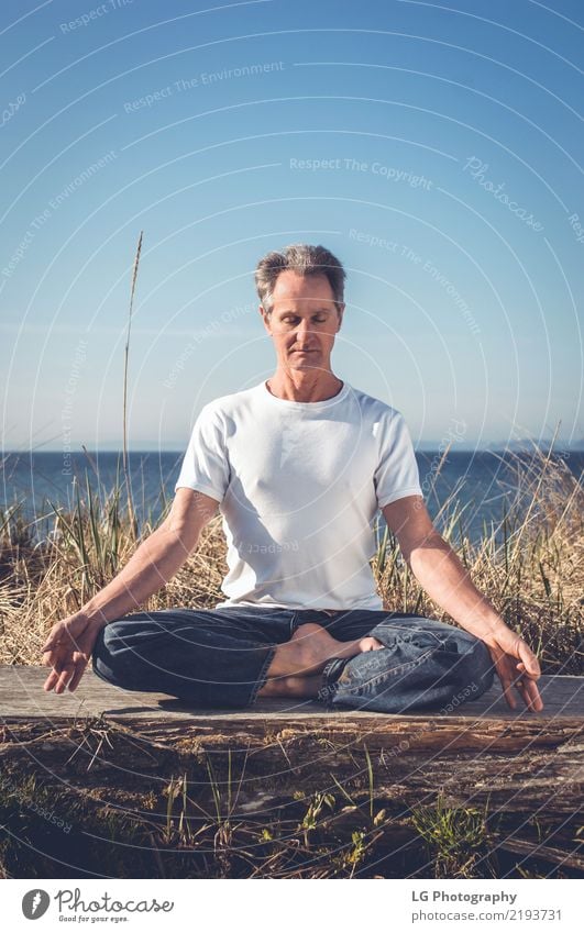 Man sitting in a relaxed yoga pose at the beach. Relaxation Meditation Sun Yoga Adults Old Sit Natural Power Serene 50-60 years Action color image