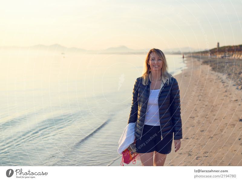 Blond smiling woman walking along beach Happy Vacation & Travel Tourism Beach Ocean Woman Adults Sand Blonde cheerful sunny Sunset Tourist conceptual Towel