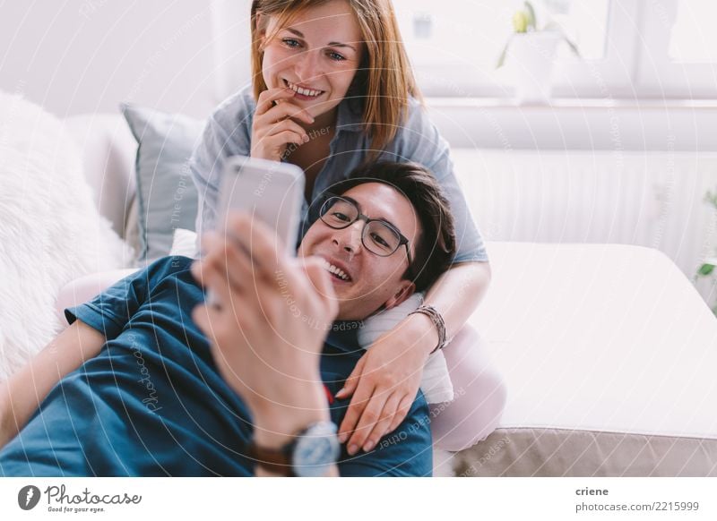 Mixe Race young adult couple watching video on phone House (Residential Structure) Living room Telephone Technology Couple Happiness asian girlfriend boyfriend